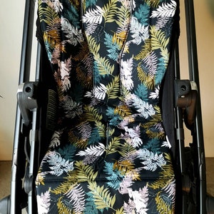 Könnte beinhalten: Ein schwarzer Kinderwagen-Sitzbezug mit einem Blatt-Muster in Grün-, Weiß- und Goldtönen.