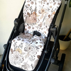 Könnte beinhalten: Ein weißer Kinderwagen-Sitzbezug mit einem floralen Muster in Braun- und Beigetönen. Der Bezug ist aus einem weichen, komfortablen Stoff gefertigt und hat ein einzigartiges Design.