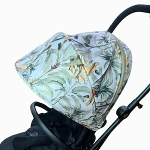 Könnte beinhalten: Ein weißer Kinderwagenhimmel mit einem tropischen Blattmuster in Grün-, Braun- und Orangetönen. Der Himmel ist aus einem weichen, atmungsaktiven Stoff gefertigt und hat einen Reißverschluss.