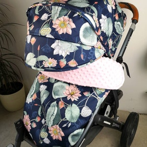 Könnte beinhalten: Ein Kinderwagen mit einem dunkelblauen und rosafarbenen floralen Verdeck und einer rosafarbenen gepolsterten Innenausstattung. Der Kinderwagen hat einen schwarzen Rahmen und schwarze Räder.