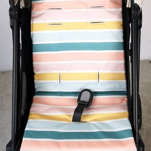 Könnte beinhalten: Ein gestreifter Kinderwagen-Sitzbezug in Rosa, Gelb, Blau und Grün. Der Bezug hat ein schwarzes Fünf-Punkt-Gurtsystem.