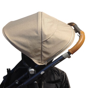 Könnte beinhalten: Ein beigefarbener Kinderwagen-Baldachin mit Reißverschluss, befestigt an einem schwarzen Kinderwagenrahmen. Der Kinderwagengriff ist aus braunem Leder. Das Wort "VISTA" ist auf dem Kinderwagenrahmen aufgedruckt.