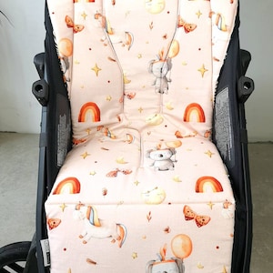 May include: A pink stroller seat cover featuring a pattern of koalas, rainbows, moons, stars, and butterflies. The cover is made from soft, comfortable fabric and is designed to fit most standard stroller seats.