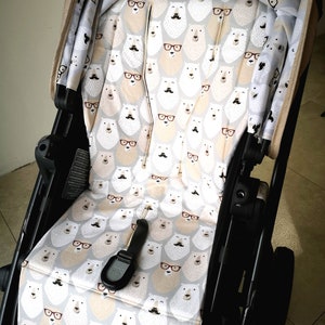 Könnte beinhalten: Ein schwarzer Kinderwagen mit einer grauen und weißen gemusterten Sitzbezug mit einem sich wiederholenden Muster von Eisbären, die Brillen und Schnurrbärte tragen.