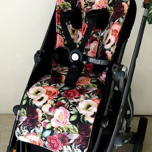 Könnte beinhalten: Ein schwarzer Kinderwagen mit einem floralen Sitzbezug. Der Bezug zeigt verschiedene rosa, rote und weiße Blumen auf schwarzem Hintergrund.
