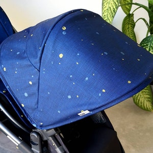 Könnte beinhalten: Ein blauer Kinderwagen-Verdeck mit einem weißen Etikett und einem Muster aus gelben und blauen Punkten.