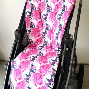 May include: A black stroller with a pink floral patterned seat liner. The liner has a white background with pink peonies and green leaves.
