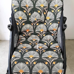 Könnte beinhalten: Ein schwarzer Kinderwagen-Sitzbezug mit einem floralen Muster mit weißen, orangefarbenen und rosa Blüten auf dunkelgrünem Hintergrund.