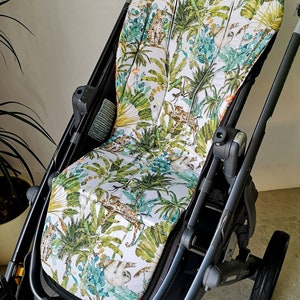 Könnte beinhalten: Ein Kinderwagen-Sitzbezug mit tropischem Dschungel-Muster mit Faultieren, Leoparden und Palmen. Der Bezug ist weiß mit grünen, braunen und orangen Akzenten.