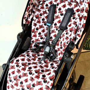 Könnte beinhalten: Ein schwarzer Kinderwagen mit einem weißen und roten Stoffbezug mit Minnie Mouse-Motiv für Sitz und Verdeck. Der Kinderwagen hat einen Fünf-Punkt-Gurt und einen schwarzen Lenker.