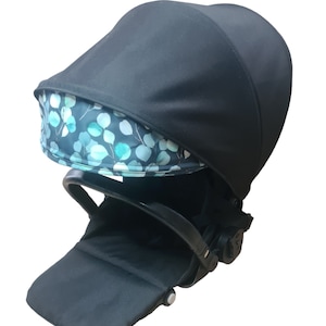 Könnte beinhalten: Schwarzer Kinderwagen-Sitz mit schwarzem Verdeck und einer abnehmbaren, gemusterten Innenausstattung mit blaugrünen und weißen Blättern auf schwarzem Hintergrund.