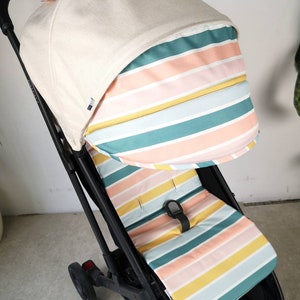 Könnte beinhalten: Ein schwarzer Kinderwagen mit einem gestreiften Verdeck und Sitzbezug. Das Verdeck ist beige mit einem hellrosa, gelben und blauen Streifenmuster. Der Sitzbezug hat ein ähnliches Streifenmuster in hellrosa, gelb und blau.