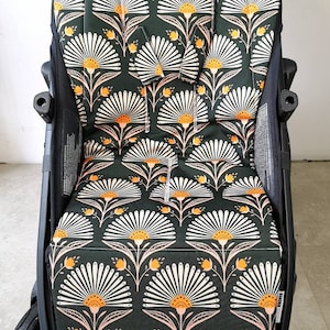 May include: A black stroller with a green, white and orange floral patterned seat cover. The cover has a white and orange flower design with a green background.