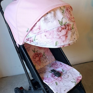 Könnte beinhalten: Ein schwarzer Kinderwagen mit einem rosa Verdeck und einer Sitzbezug mit Blumenmuster. Der Kinderwagen hat einen schwarzen Griff und Räder.