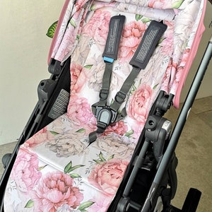 Può includere: Un rivestimento per seggiolino passeggino con un motivo floreale con peonie rosa e bianche. Il rivestimento è realizzato in un tessuto morbido e confortevole ed è progettato per adattarsi alla maggior parte dei seggiolini passeggino standard.