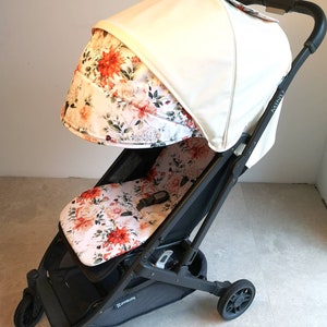 Könnte beinhalten: Ein schwarzer Kinderwagen mit einem weißen Verdeck und einer Sitzbezug mit Blumenmuster. Der Kinderwagen hat einen schwarzen Griff und schwarze Räder.