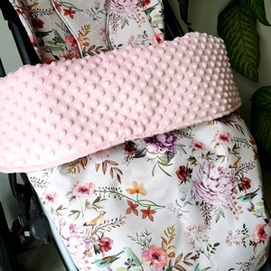Könnte beinhalten: Ein rosa-weißer Fußsack für einen Kinderwagen mit Blumenmuster und einem rosa Fleecefutter. Der Fußsack ist so konzipiert, dass ein Baby in einem Kinderwagen warm und gemütlich bleibt.
