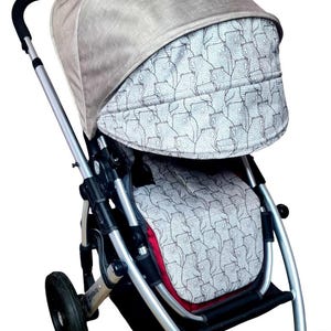 Könnte beinhalten: Ein grauer Kinderwagen mit schwarzem Gestell und schwarzen Rädern. Der Kinderwagen hat ein graues und weißes gemustertes Verdeck und einen grauen und weißen gemusterten Sitz.