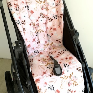 Könnte beinhalten: Ein rosa Kinderwagen-Sitzbezug mit einem Blumenmuster mit braunen, weißen und rosa Blumen und Blättern. Der Bezug ist aus weichem, bequemem Stoff gefertigt und passt auf die meisten Standard-Kinderwagen-Sitze.