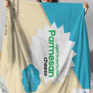 May include: A beige and blue blanket with a white circle in the center. The circle has green text that says "Parmesan cheese" and "aged to perfection". The blanket also has a blue cloud with the text "Great source of humor".