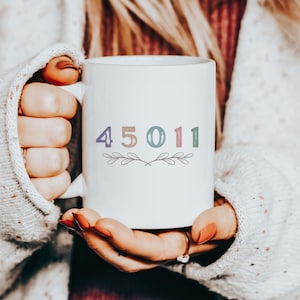 May include: White ceramic mug with a colorful design featuring the numbers 45011 and a small floral motif.