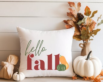 May include: White throw pillow with the text "hello fall" in red and green lettering. The pillow is decorated with a small orange and green squash.