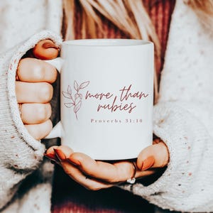May include: White ceramic mug with a pink floral design and the text "more than rubies Proverbs 31:10" in pink.