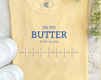 May include: A yellow t-shirt with the text "SALTED BUTTER" and "NET WT. 4oz (113g)" printed in blue. The shirt also has a measurement guide in tablespoons printed in blue.