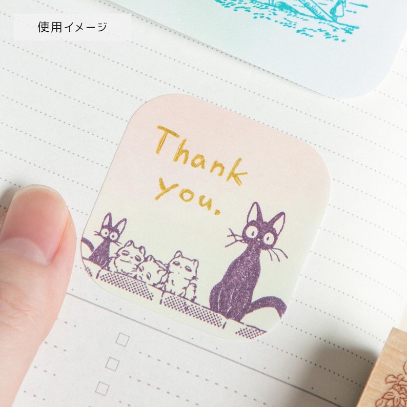 May include: A square sticker with rounded corners, featuring a gradient background of pink and light green. The sticker has the words "Thank you" in gold script, and a row of cartoon cats in purple.
