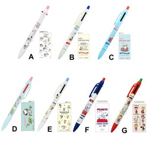 May include: Collection of seven Peanuts-themed ballpoint pens. Each pen features a different color scheme and design, with illustrations of Snoopy, Woodstock, and other characters. The pens are accompanied by matching design cards.