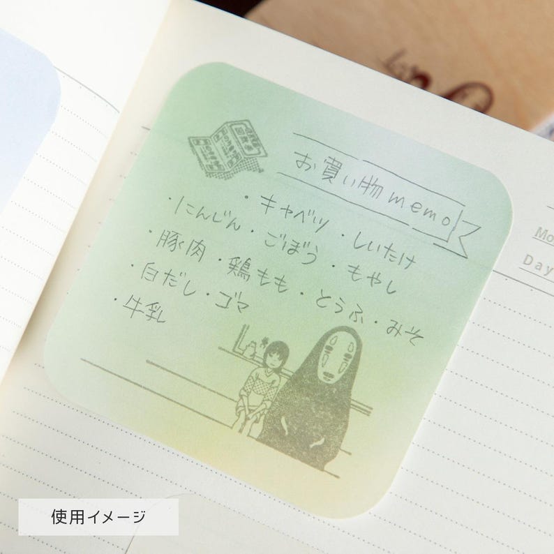 May include: A light green sticky note with Japanese text and illustrations. The note features a newspaper graphic, a list of items, and a drawing of two characters. The text includes the words "お買い物 memo" and "使用イメージ".