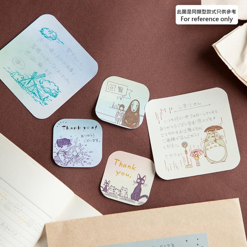 May include: A collection of square and diamond-shaped stickers with illustrations and handwritten text. Designs include anime characters, a windmill, and the words "Thank you." Colors are pastel with a brown background.