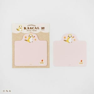 May include: A set of pink sticky notes with a cartoon raccoon illustration. The packaging reads "RAScal 20 Sticky Notes". The notes have a scalloped top and a small cake graphic at the bottom. The background is white.