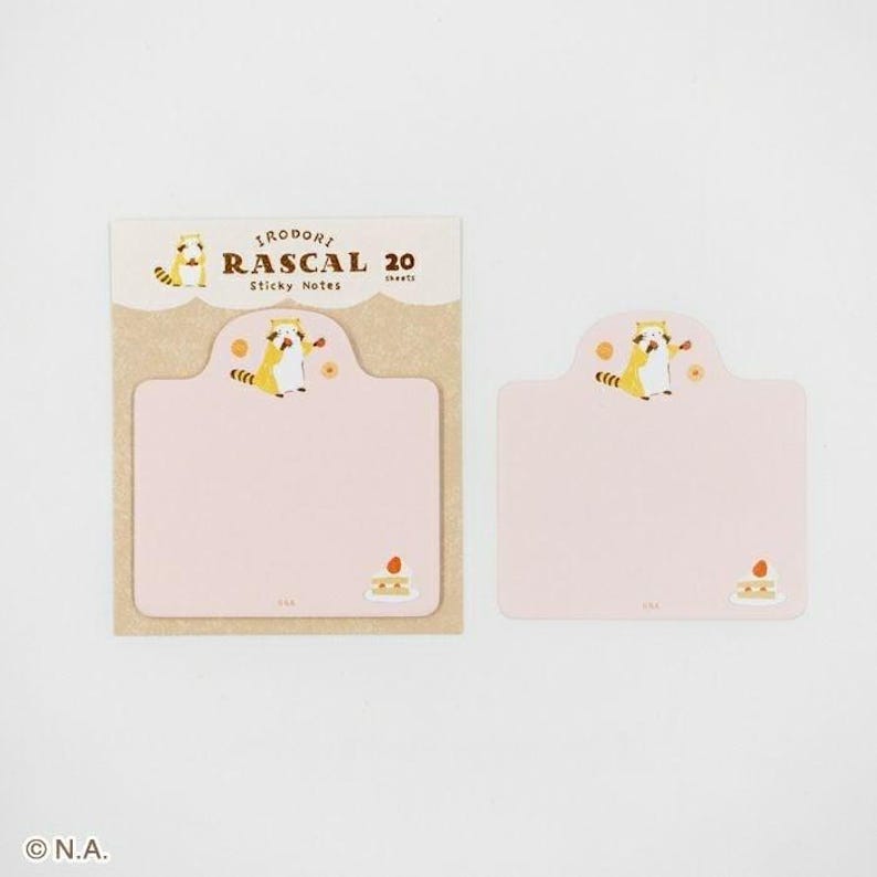 May include: A set of pink sticky notes with a cartoon raccoon illustration. The packaging reads "RAScal 20 Sticky Notes". The notes have a scalloped top and a small cake graphic at the bottom. The background is white.