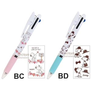 Puede incluir: Dos bol&iacute;grafos multicolores con dise&ntilde;os de Snoopy. Un bol&iacute;grafo tiene un cuerpo rosa y el otro azul claro. Ambos bol&iacute;grafos tienen la parte superior blanca y el texto "YOU GOT A LOVE LETTER?" impreso. Cada bol&iacute;grafo tiene una tarjeta a juego con ilustraciones de Snoopy.