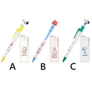 May include: Three different colored pens with a Peanuts character on top. The pens are yellow, blue, and green. Each pen has a small white card attached to it with a Peanuts character and the text "PEANUTS" printed on it. The text "軸デザイン" is printed on each card.