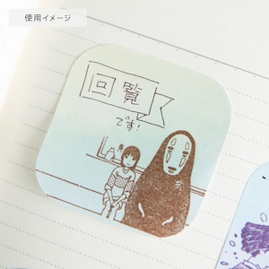 May include: A light blue, square-shaped sticky note with a brown illustration of characters from a Japanese animated film. The note has Japanese text and is placed on a lined paper background.