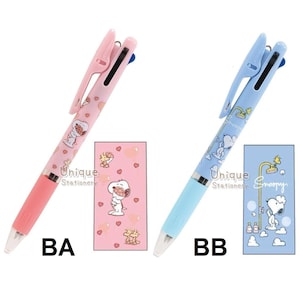Puede incluir: Dos bol&iacute;grafos multicolores con dise&ntilde;os de Snoopy y blocs de notas a juego. Un bol&iacute;grafo es rosa con un bloc de notas rosa, y el otro es azul claro con un bloc de notas azul claro. Los bol&iacute;grafos tienen el texto "Unique Stationery".