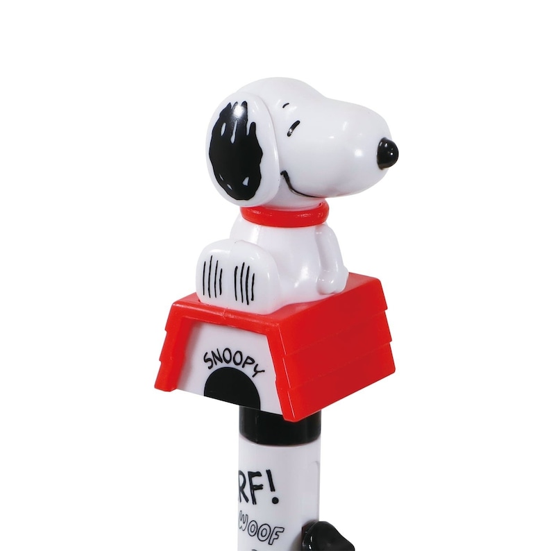 May include: A white plastic pen with a red and white doghouse topper. The doghouse has the word "Snoopy" printed on it. A white plastic figure of Snoopy is sitting on top of the doghouse. The pen has the words "Woof!" and "R.F!" printed on it.