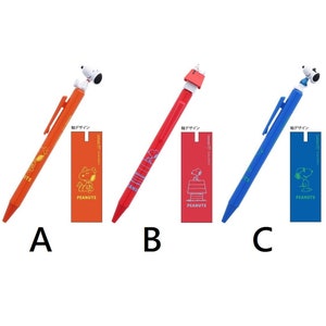 May include: Three different colored pens with Peanuts characters on the top. The pens are orange, red, and blue. Each pen has a small rectangular tag attached to it with the Peanuts logo and the text "Peanuts" in white. The tags also have the text "絵デザイン" in Japanese.