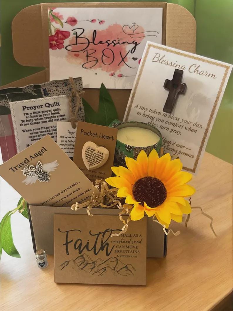 May include: A Blessing Box filled with inspirational items. Includes a candle, a sunflower, a cross charm, a pocket heart, a travel angel, and a card with the word "Faith" and a mountain illustration. The box also contains a "Prayer Quilt" card.