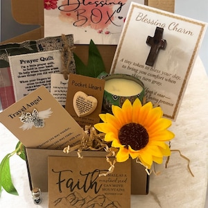 May include: A Blessing Box filled with inspirational items. Includes a wooden cross charm, a sunflower, a candle, and cards with uplifting messages. The box is decorated with floral accents and the words "Blessing Box" in script.