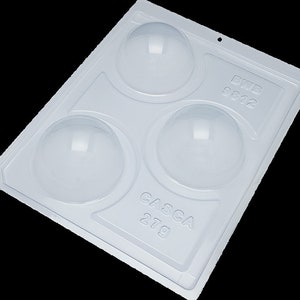 May include: A white plastic mould with four round cavities for making chocolate spheres. The mould has the text "CASCA 27g" and "B112 9812" printed on it.