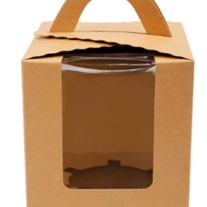 Puede incluir: Una caja de cartón marrón con una ventana transparente y un asa. La caja está diseñada para empaquetar y exhibir productos de panadería.