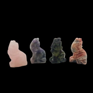 May include: Five carved crystal animal figurines, each in a different color. The figurines are arranged in a row from left to right: pink, purple, green, and red. The figurines are all in the shape of a wolf.
