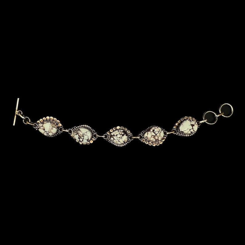 K&ouml;nnte beinhalten: Silberarmband mit f&uuml;nf tropfenf&ouml;rmigen Steinen mit gesprenkeltem Muster. Die Steine sind in einer Silberfassung mit einem Perlenrand gefasst. Das Armband hat einen Knebelverschluss.