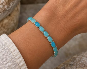 May include: A silver-toned bracelet featuring a series of oval-shaped, light blue cabochon stones set in individual metal prongs. The bracelet wraps around the wrist, showcasing a continuous line of smooth, polished blue gemstones linked together.