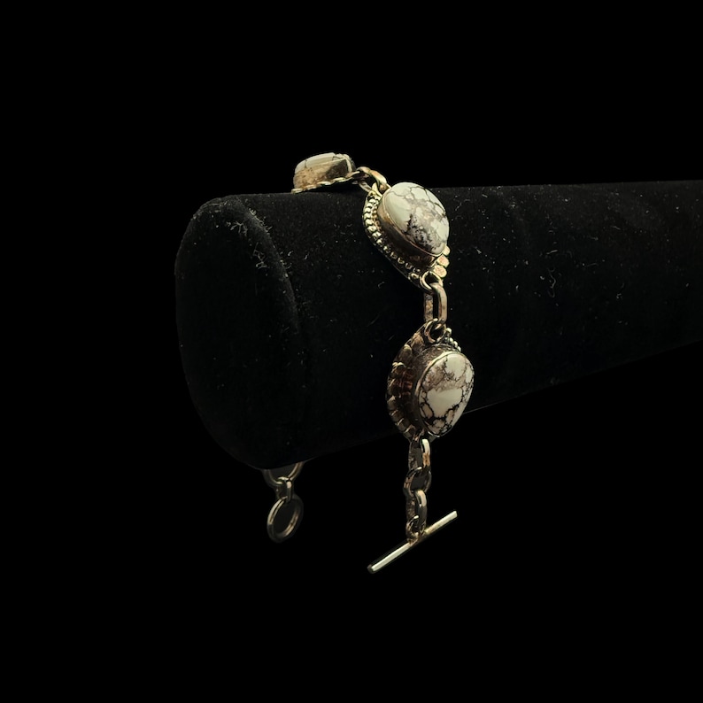 K&ouml;nnte beinhalten: Silberarmband mit drei ovalen, wei&szlig;-grauen Steinen. Die Steine sind in einem dekorativen Silberrahmen gefasst und durch silberne Glieder verbunden. Das Armband hat einen Knebelverschluss.