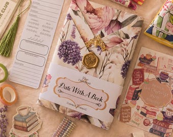 May include: A gift-wrapped book featuring a floral pattern, a gold wax seal, and a paper band labeled Date With A Book. The set includes a book review card, a green tassel bookmark, stickers, colorful sticky tabs, and assorted snacks and candies.