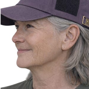 May include: A purple baseball cap with a black square patch on the side. The cap has a curved brim and a gold-colored metal detail on the side. The cap is made of a soft, durable material.